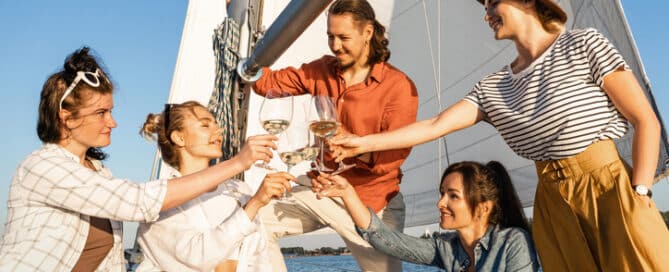 Group of happy friends drinking wine and relaxing on the sailboat during sailing in sea.